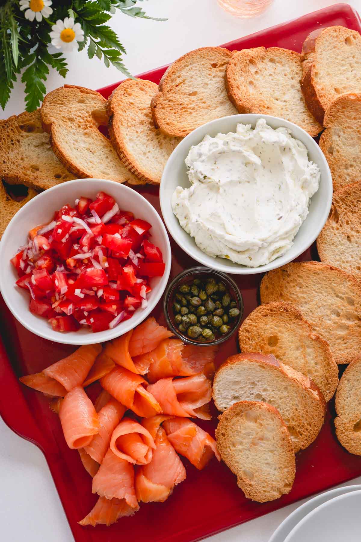 A platter of crostini, smoked salmon, and bowls of cream cheese spread, tomato relish and capers.
