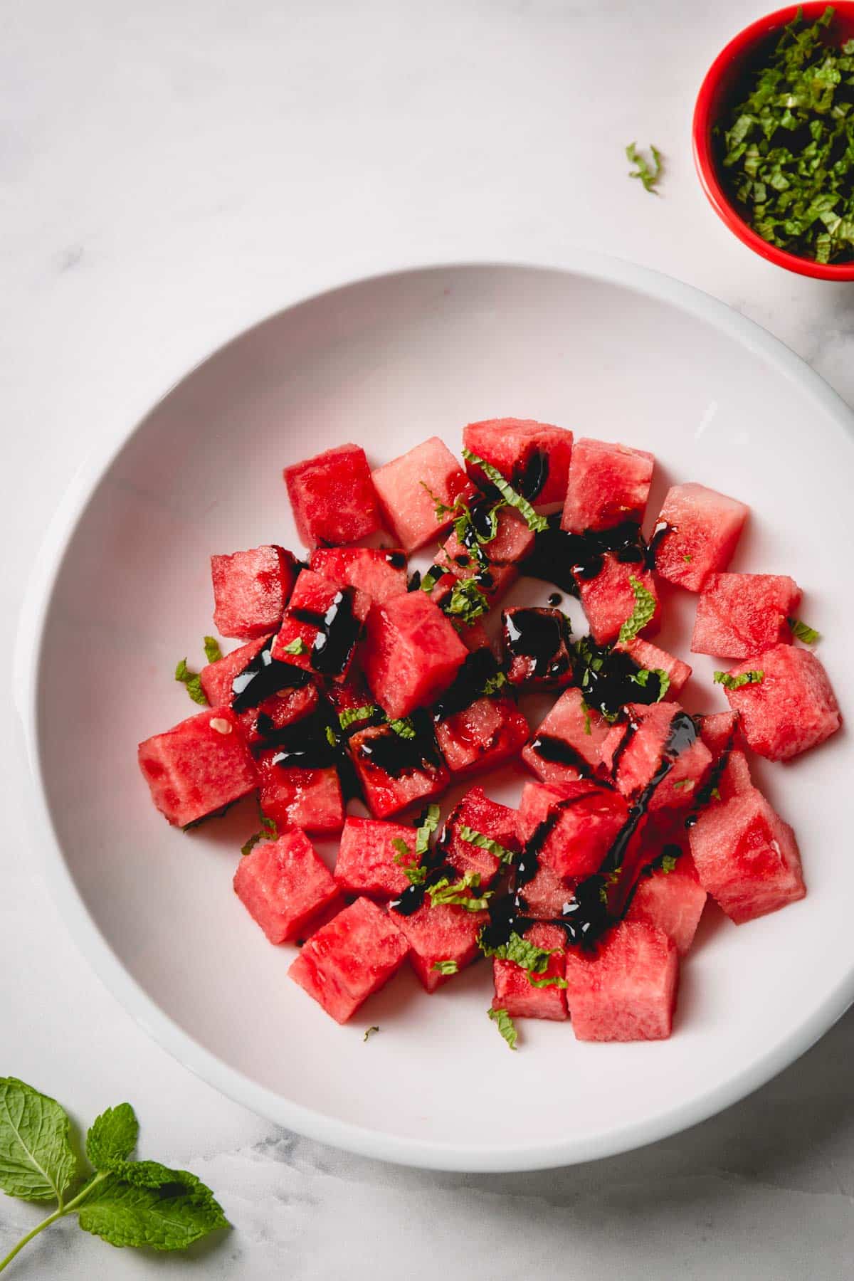 Cubed watermelon in a white bowl topped with balsamic glaze and chopped fresh mint.