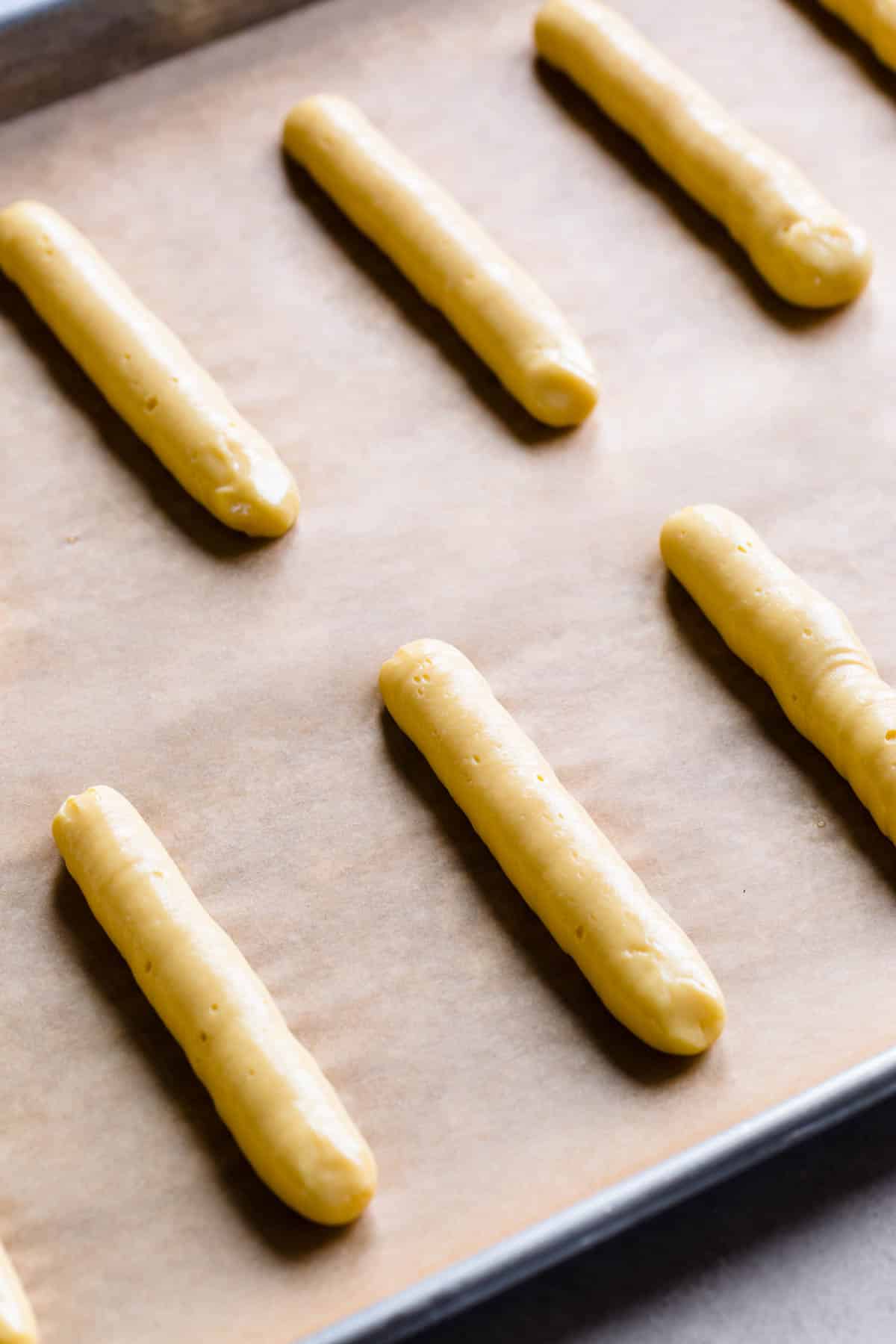 Choux dough piped into skinny logs on a baking sheet lined with parchment paper.