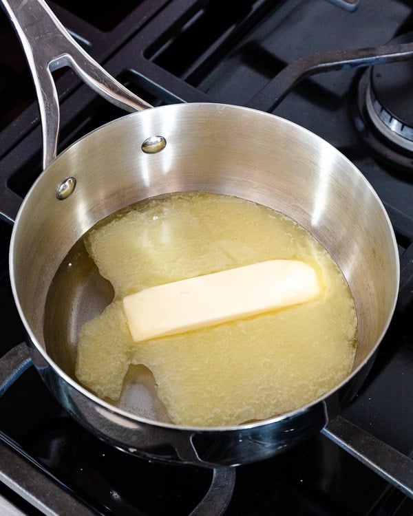 A stick of butter and water in a stainless steel saucepan.