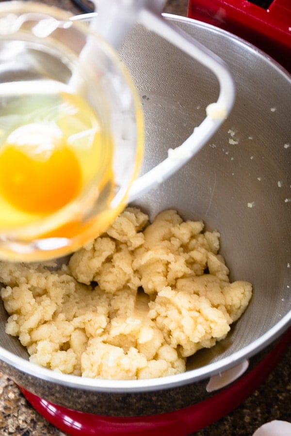 One egg is being added into a shaggy dough in a mixing bowl with paddle attachment.