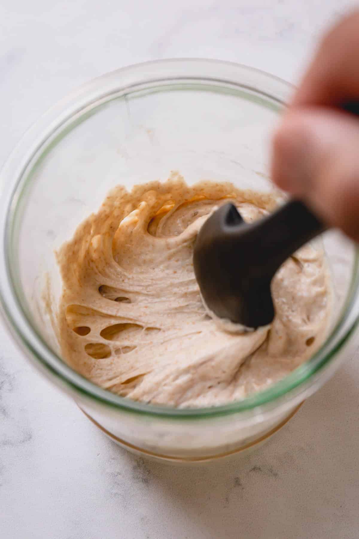 Scooping sourdough starter with a black silicone spatula.
