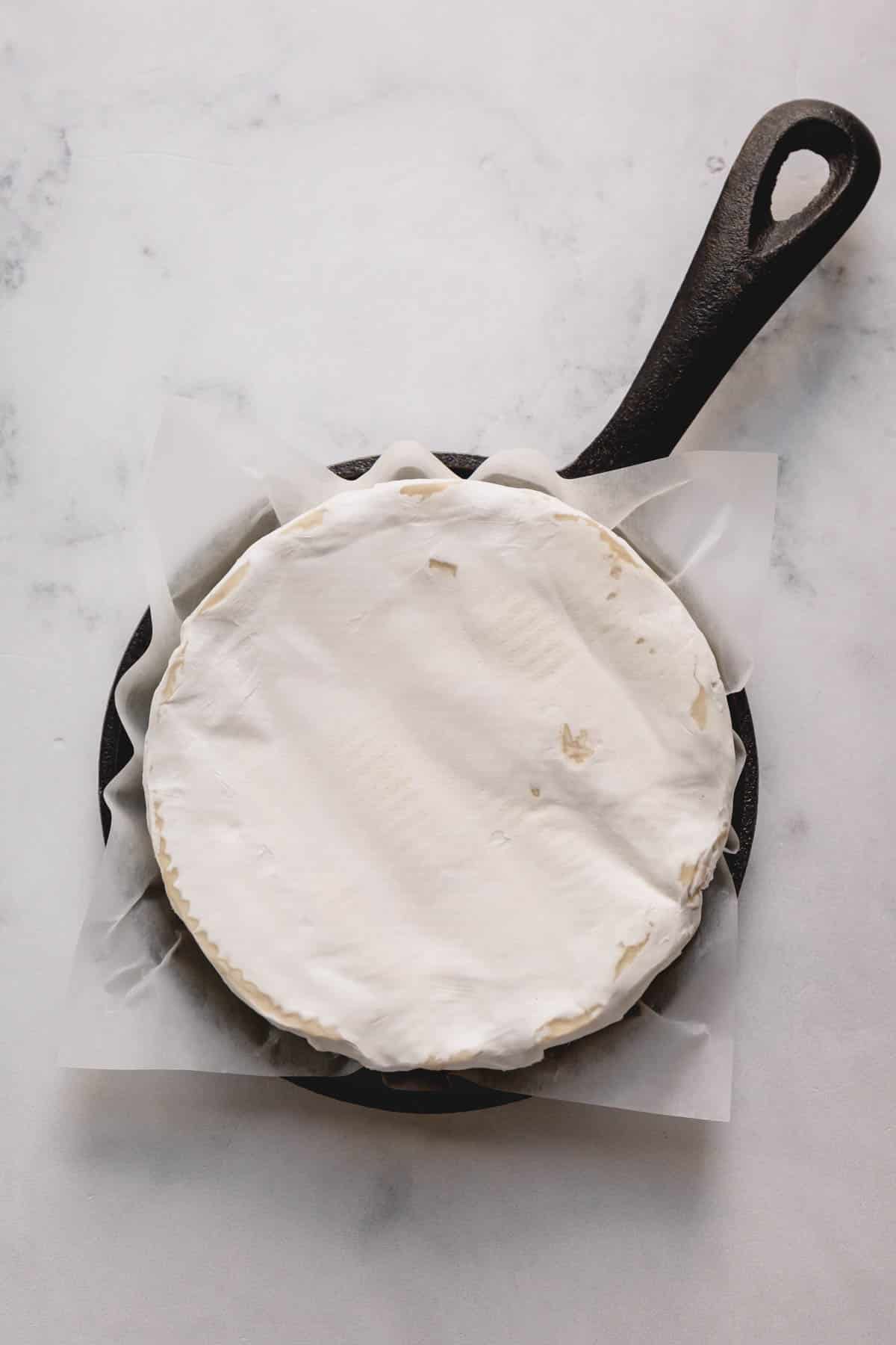 A wheel of brie in a small cast iron skillet lined with parchment paper.