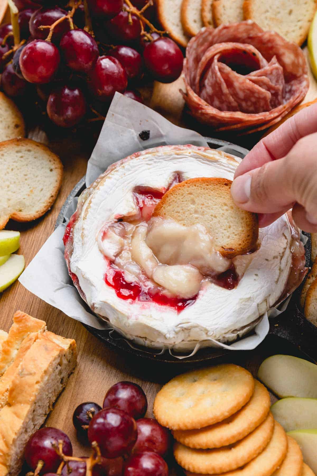 A wheel of baked raspberry brie with baguette chip dipped in the center.