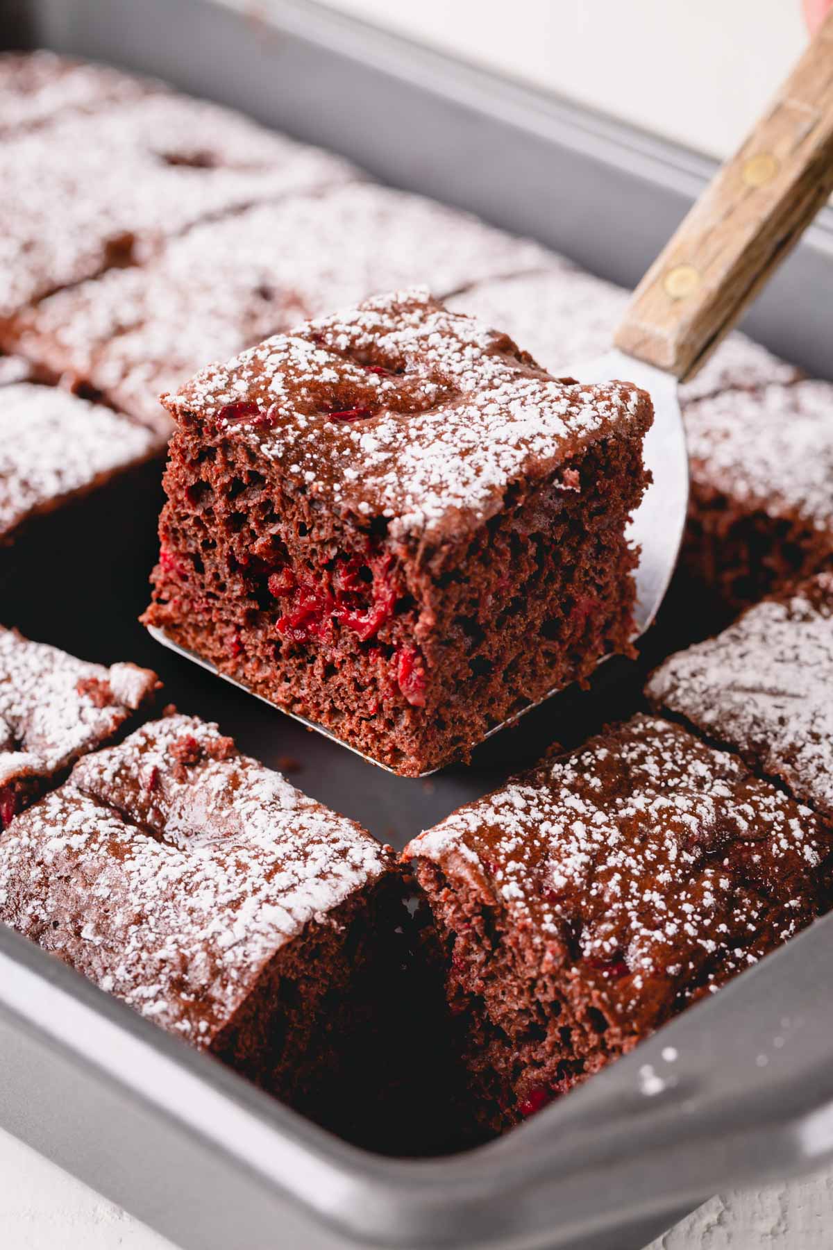 Chocolate cherry cake in a baking pan with one slice lifted.