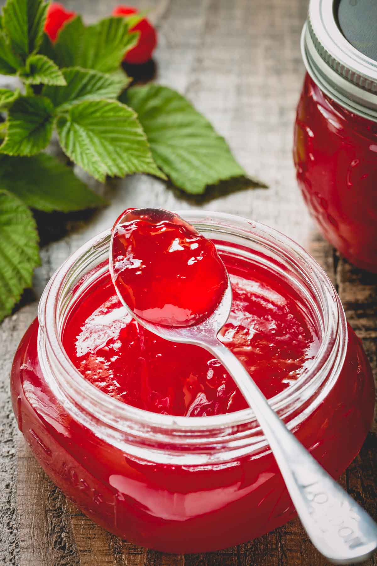 Raspberry jelly in a wide mouth glass jar with spoonful of jelly rested on the jar.