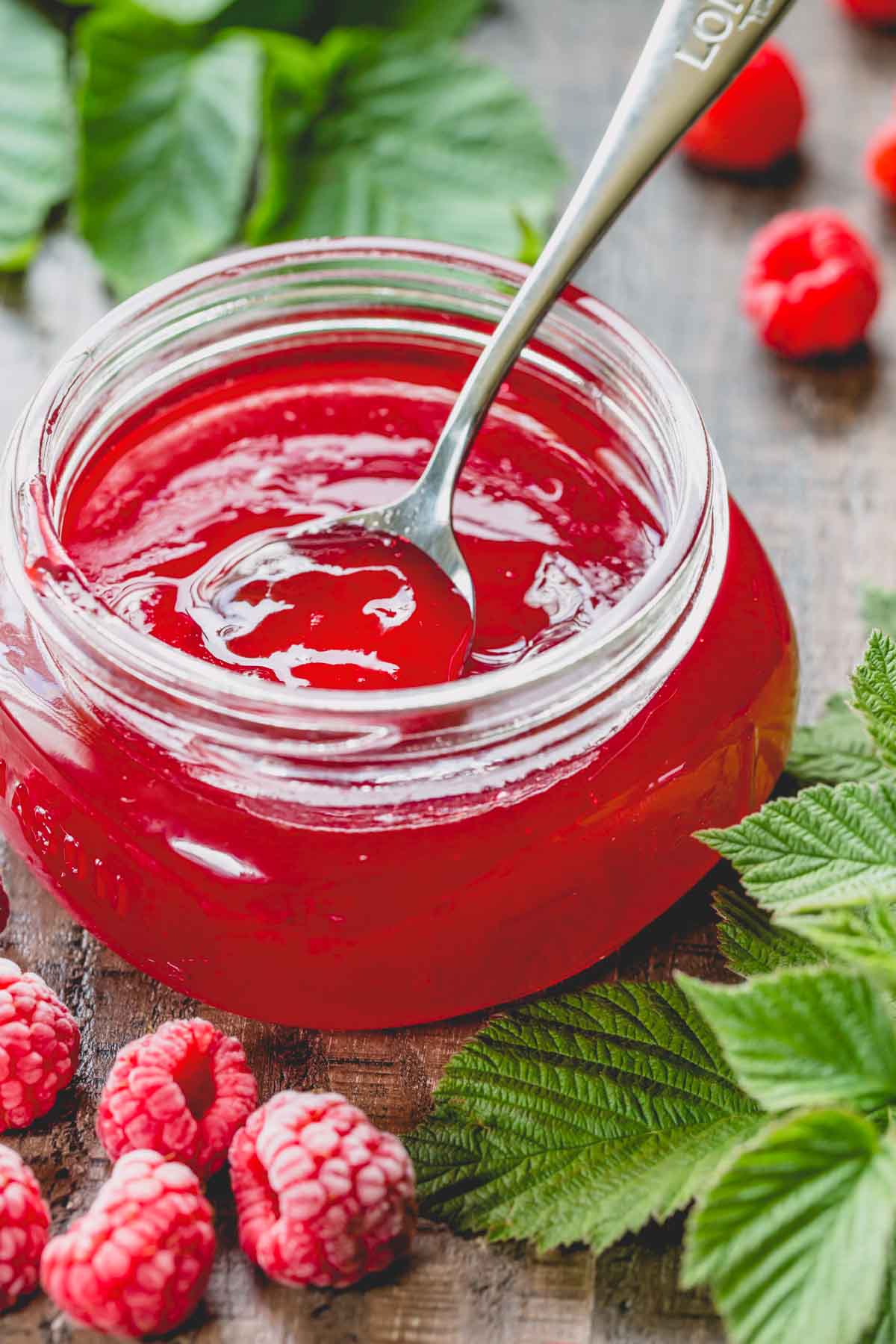 A glass jar of raspberry jelly with a spoon dip in it.