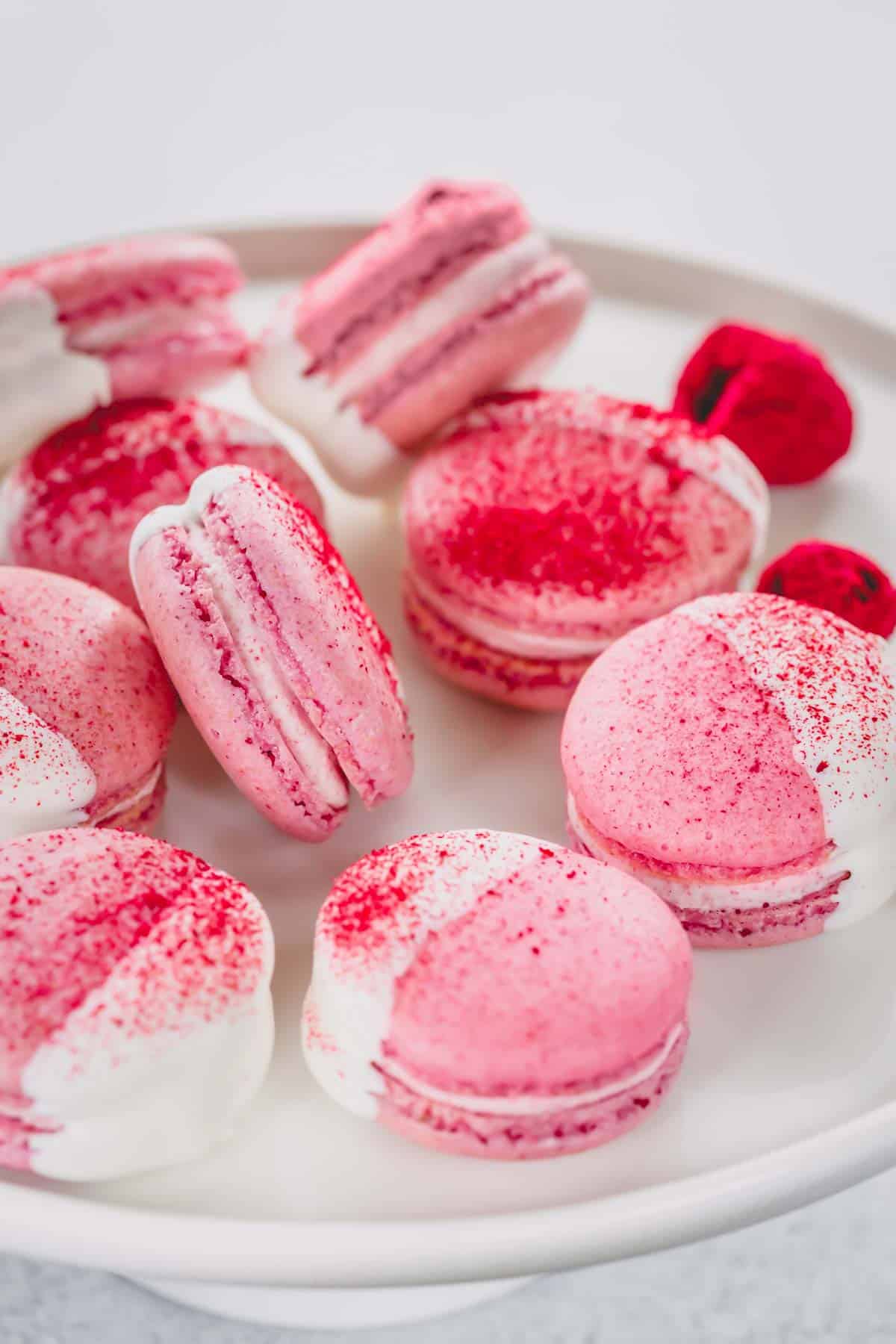 White chocolate dipped raspberry macarons arranged on a white platter.