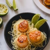 3 seared scallops over a bed of spaghetti and garnished with lime wedges.
