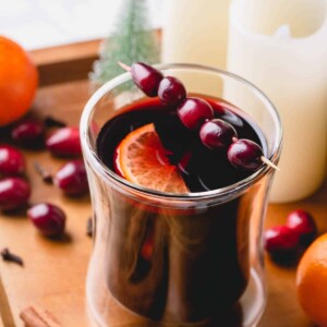 Mulled wine in a glass garnished with fresh cranberries and slice of orange.