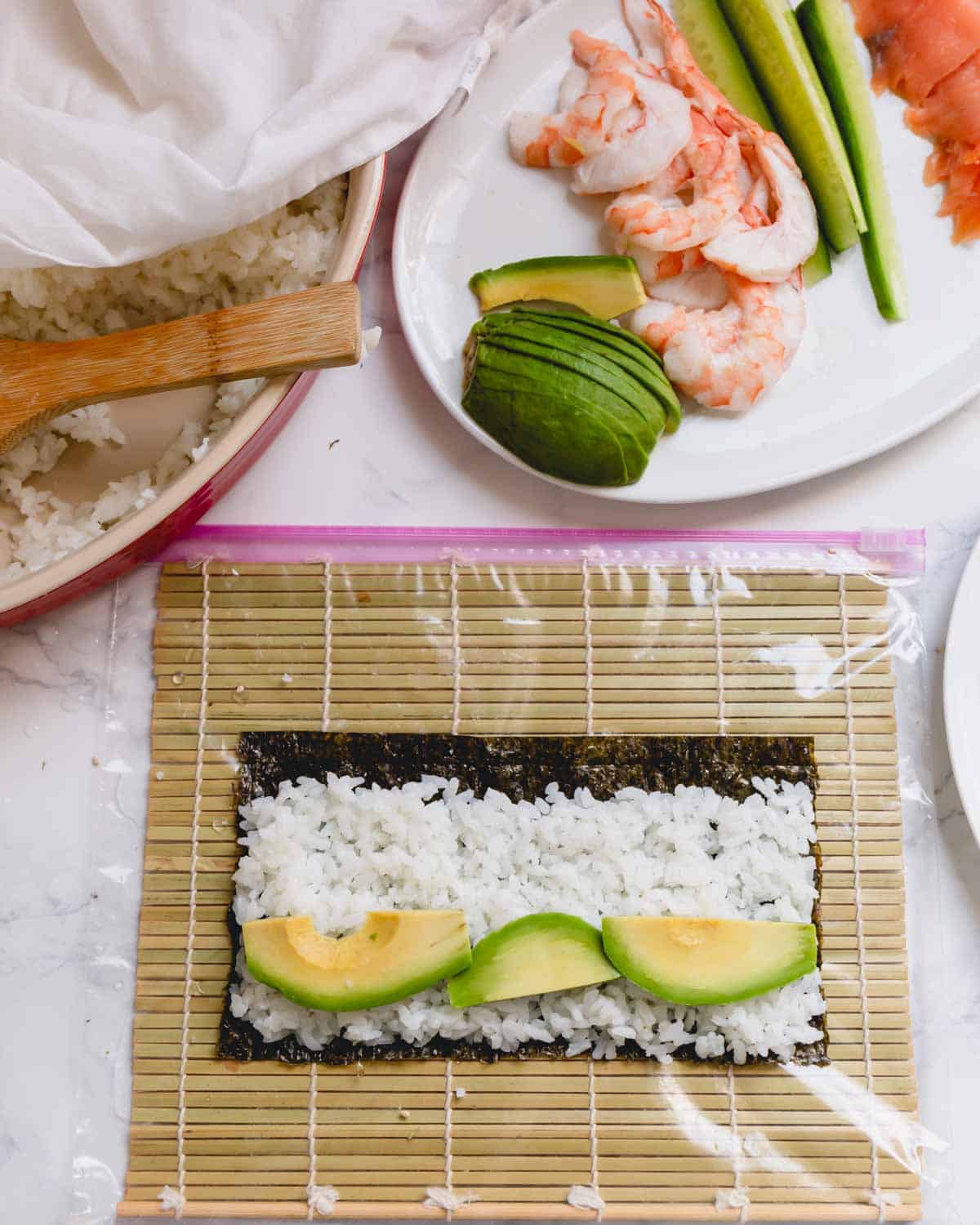 Nori sheet with rice and avocado slices on a bamboo mat.