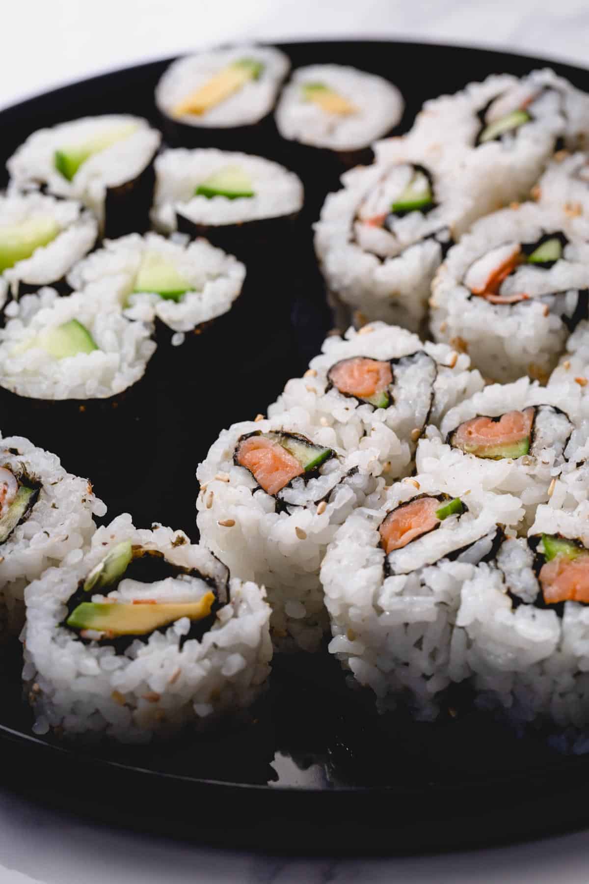 Variety of homemade sushi rolls on black round platter.
