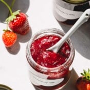 Strawberry jam in a glass jar with a spoon in the jar.