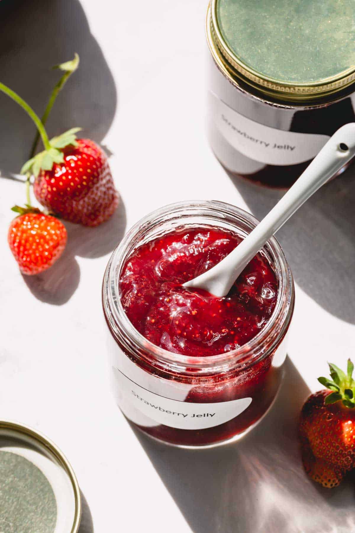Strawberry jam in a glass jar with a spoon in the jar.