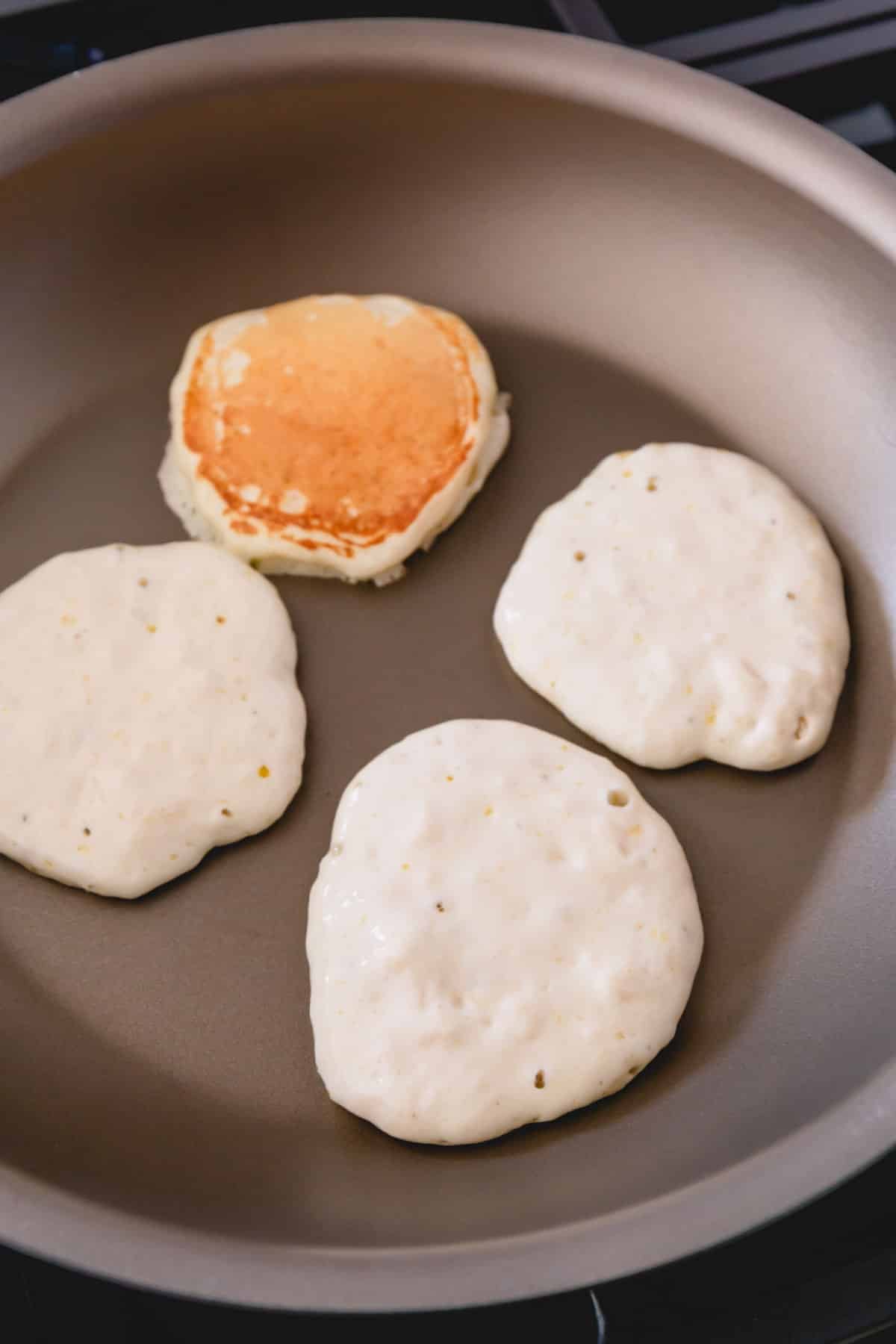 Four pancakes in a skillet one flipped over.