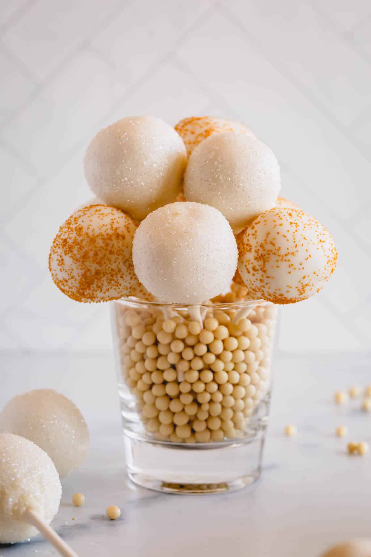 gold and white cake pops in a glass.