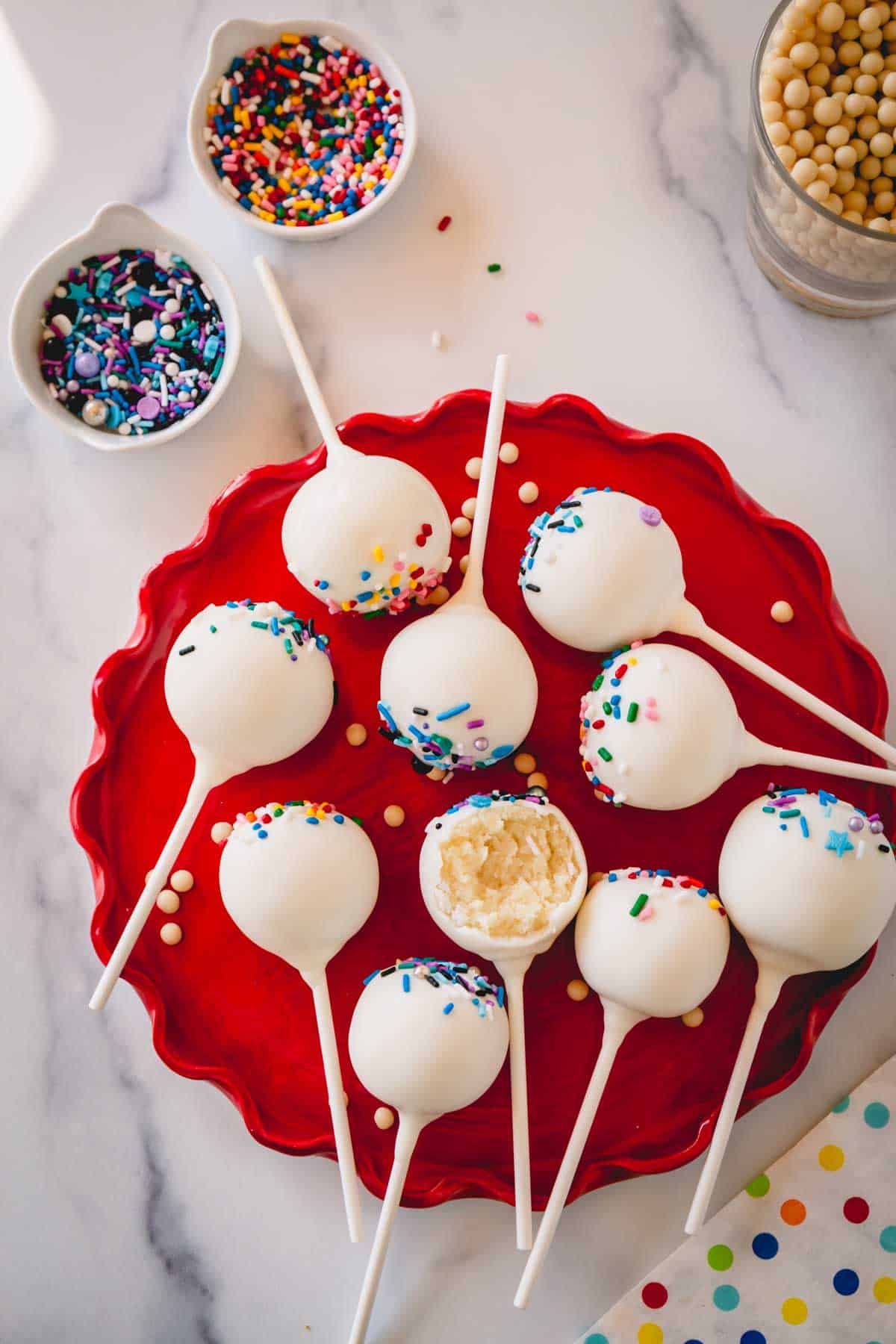 Cake pops with sprinkles on a red plate.