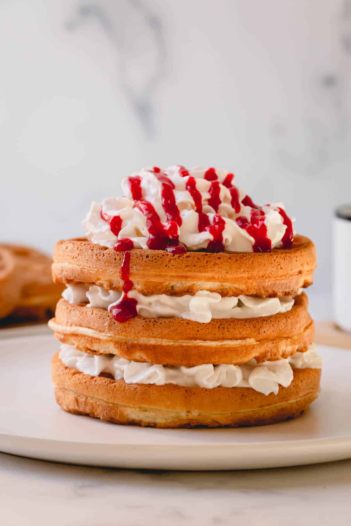 a stack of waffles with whipped cream and raspberry sauce.