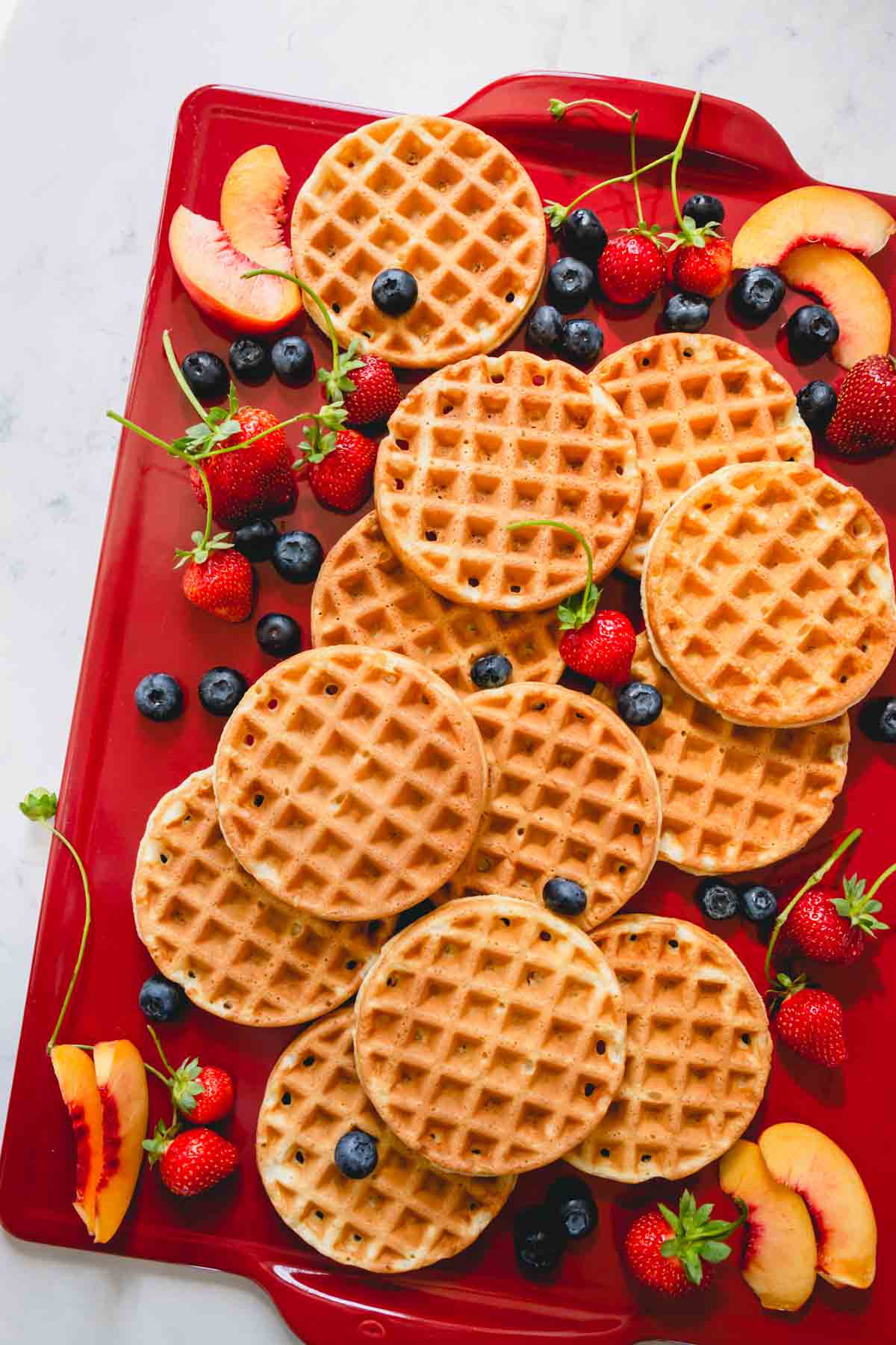 Waffles on a red serving board with fresh berries.