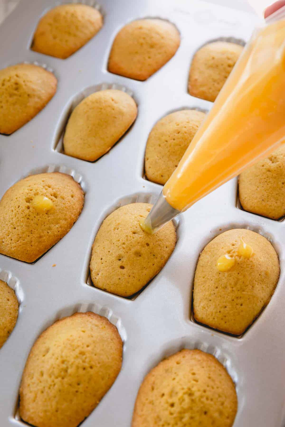 piping lemon curd into baked madeleines