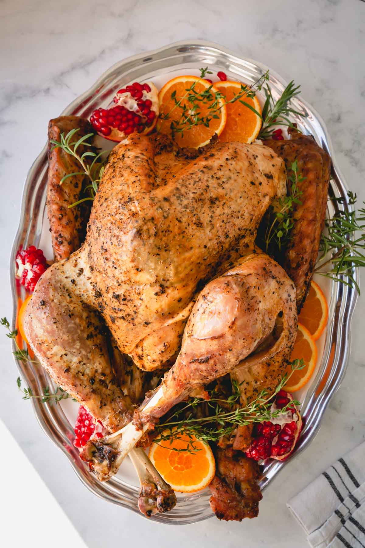 Whole roast turkey on a silver platter garnished with orange slices, pomegranate halves and fresh herbs.