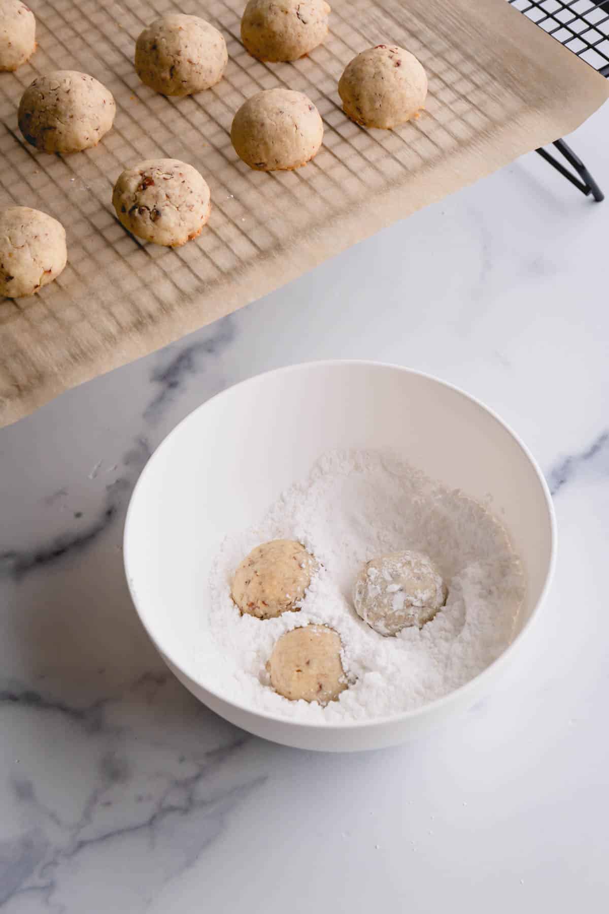 snow ball cookies dropped in a bowl of powdered sugar.