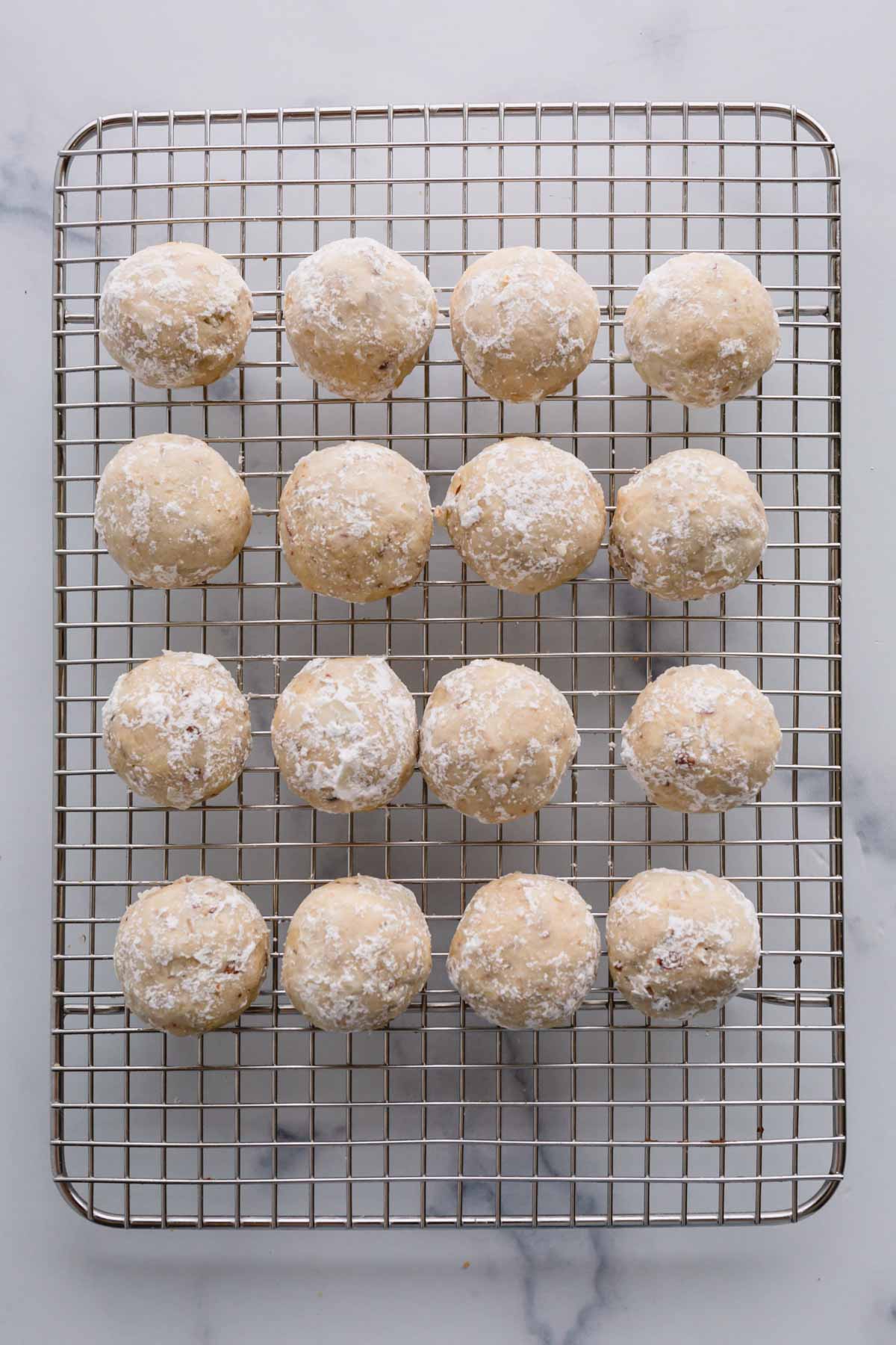 snowball cookies rolled in powedered sugar once and arranged on a wire rack.