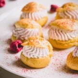 Mini raspberry cream puffs on a white platter dusted with freeze-dried raspberry powder.