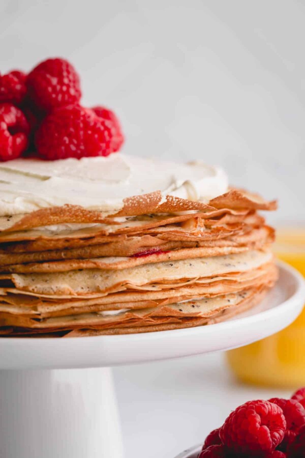 a crepe cake with whipped cream and raspberries on top.