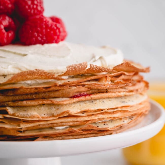 a crepe cake with whipped cream and raspberries on top.