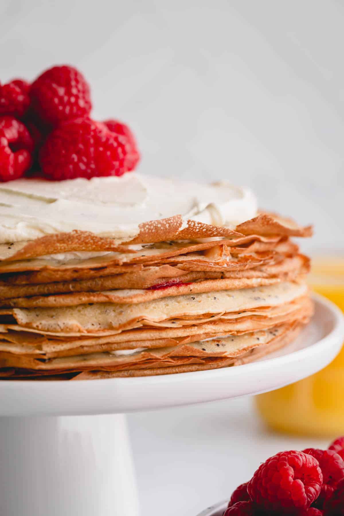 a whole crepe cake with whipped cream and raspberries on top.