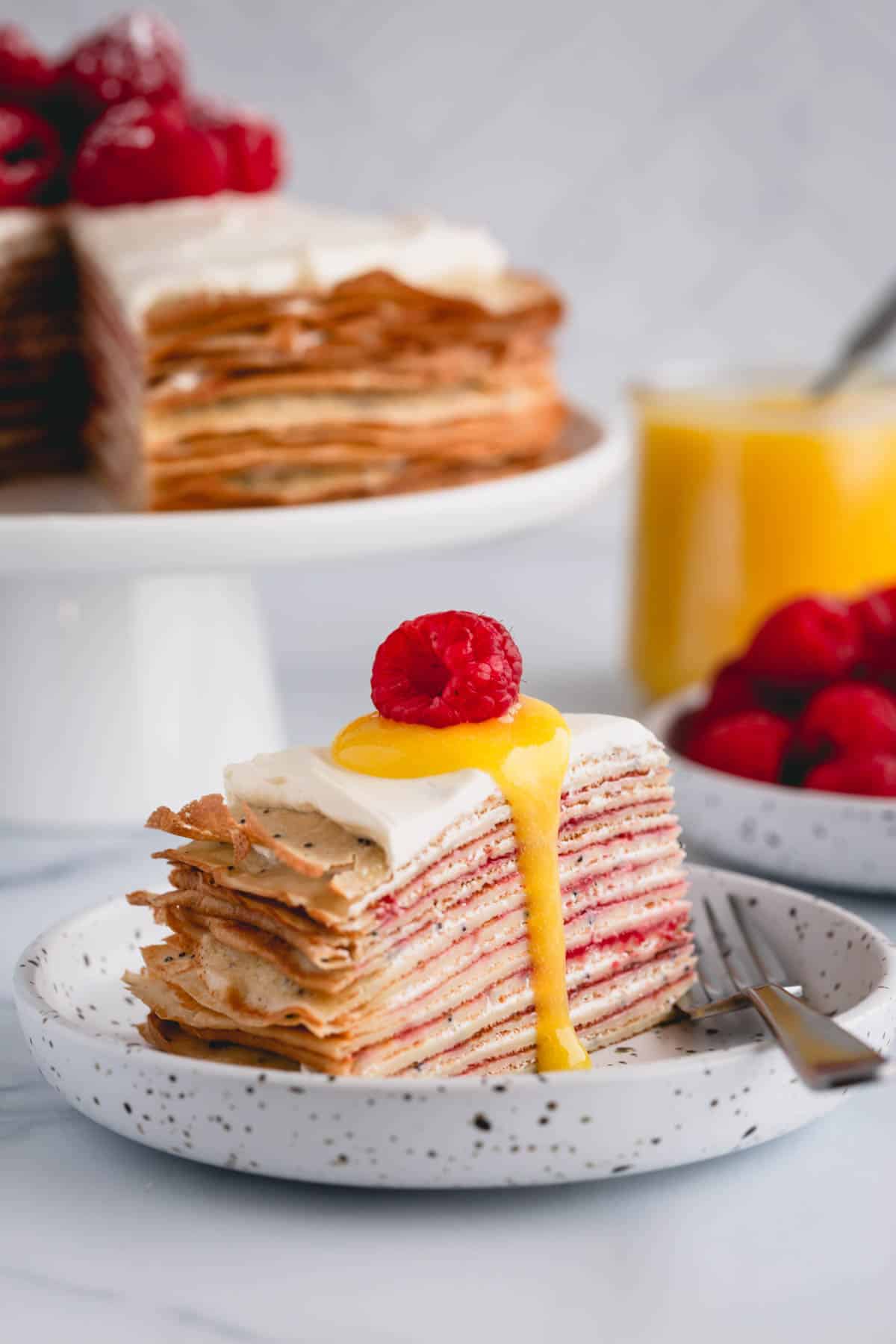 a slice of crepe cake topped with lemon curd and raspberries on top.