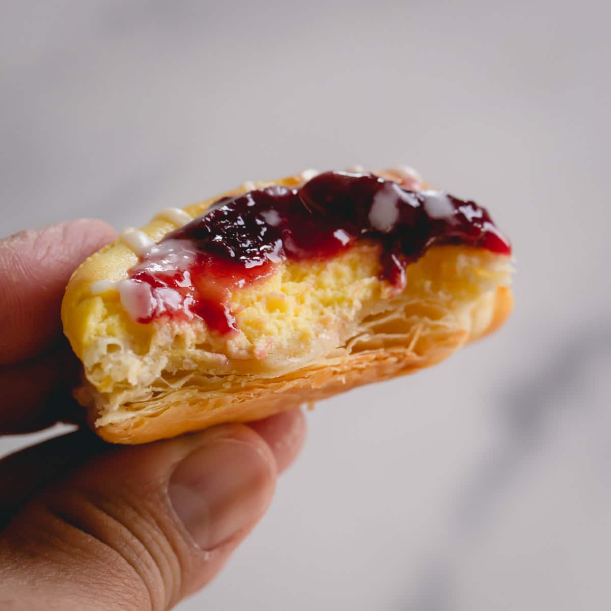 A hand holding a cherry danish with a bite missing exposing the cream cheese center.