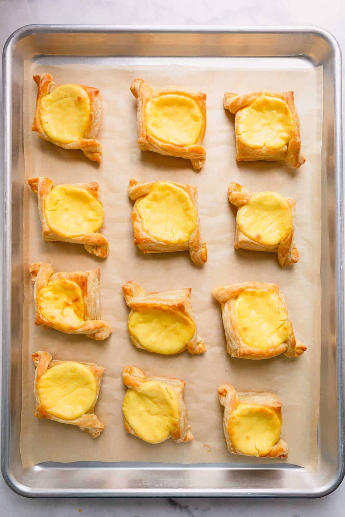 Baked puff pastry danishes with a cream cheese filling on a parchment paper-lined baking sheet.