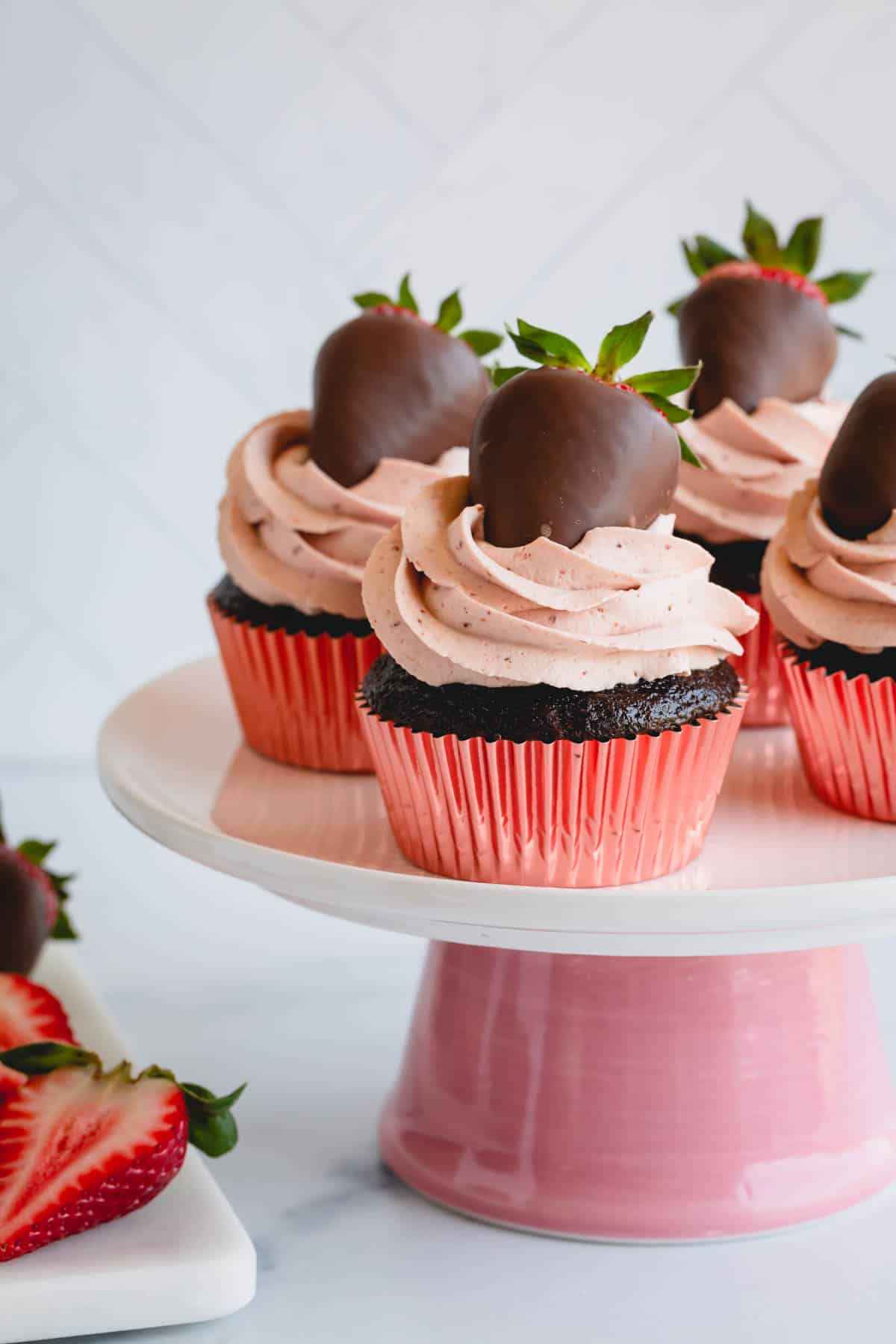 Strawberry chocolate cupcakes topped with chocolate covered strawberries on a cake stand.