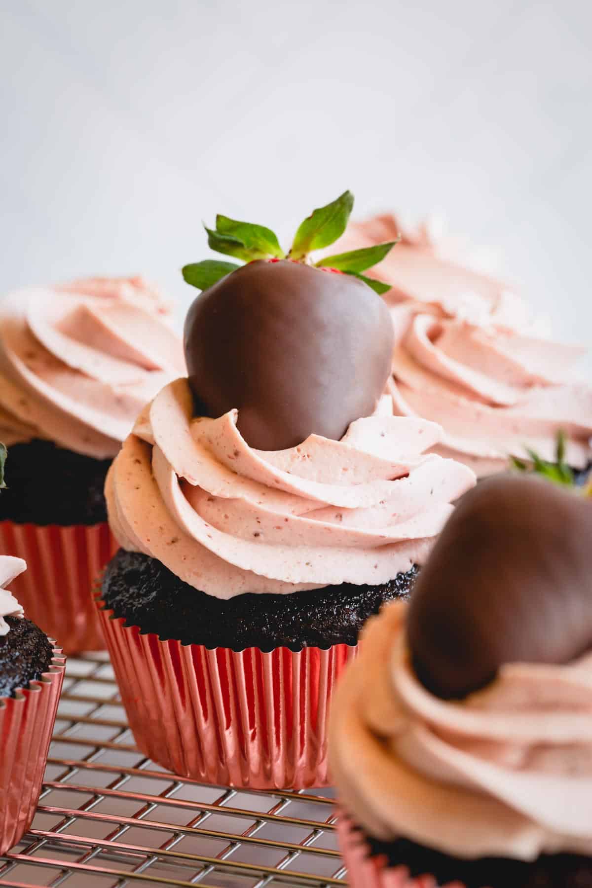 Side view of strawberry chocolate cupcakes topped with chocolate covered strawberries on a wire rack.