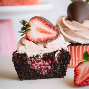 A strawberry chocolate cupcake topped with a chocolate strawberry sliced in half exposing the strawberry filling.