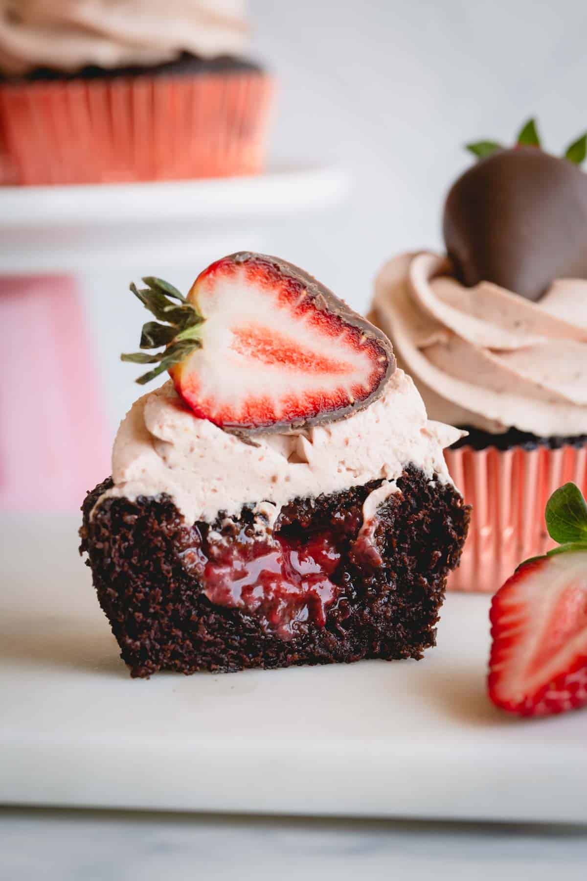 A strawberry chocolate cupcake topped with a chocolate strawberry sliced in half exposing the jam filling.