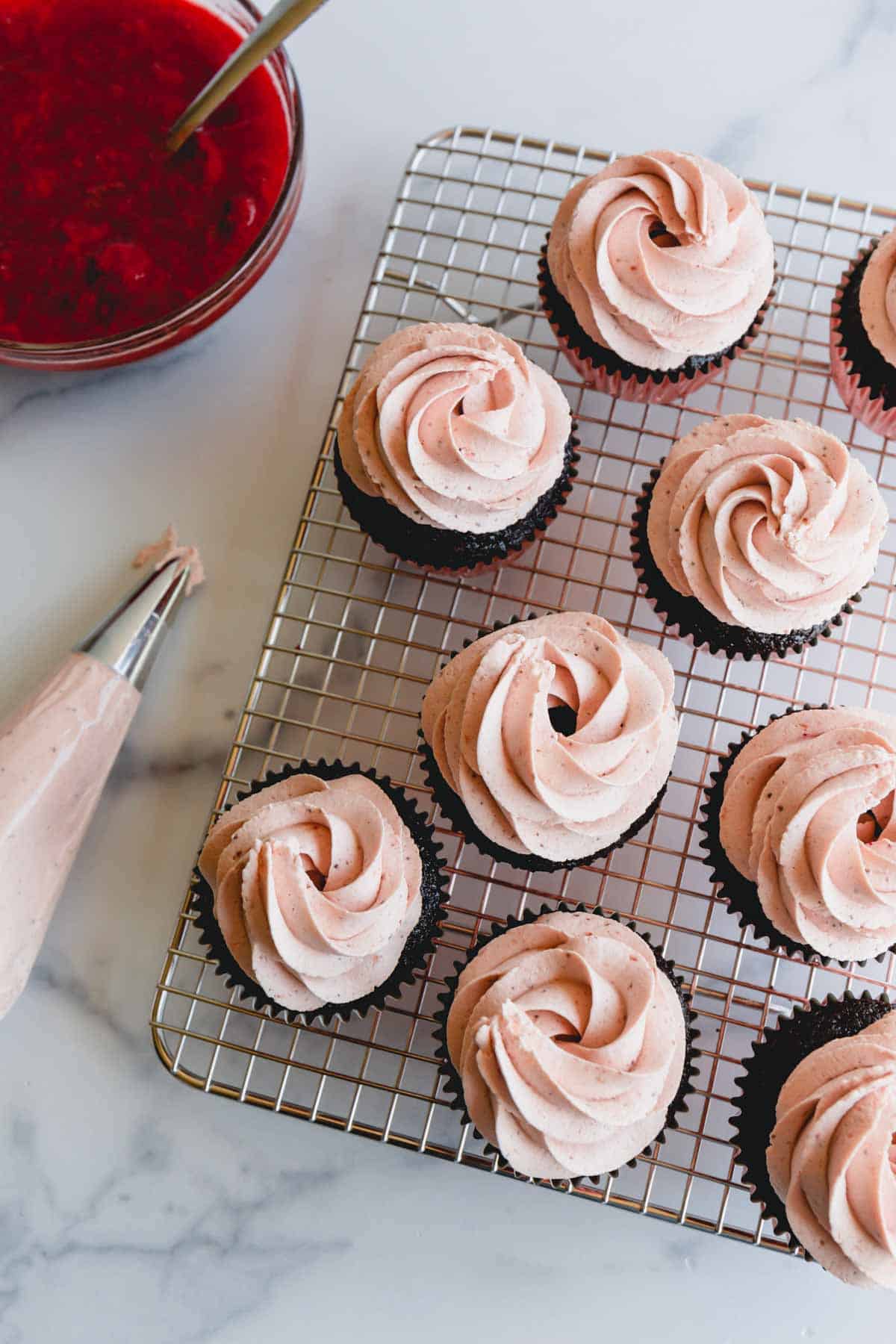 Strawberry chocolate cupcakes topped with strawberry whipped cream frosting on a wire rack.