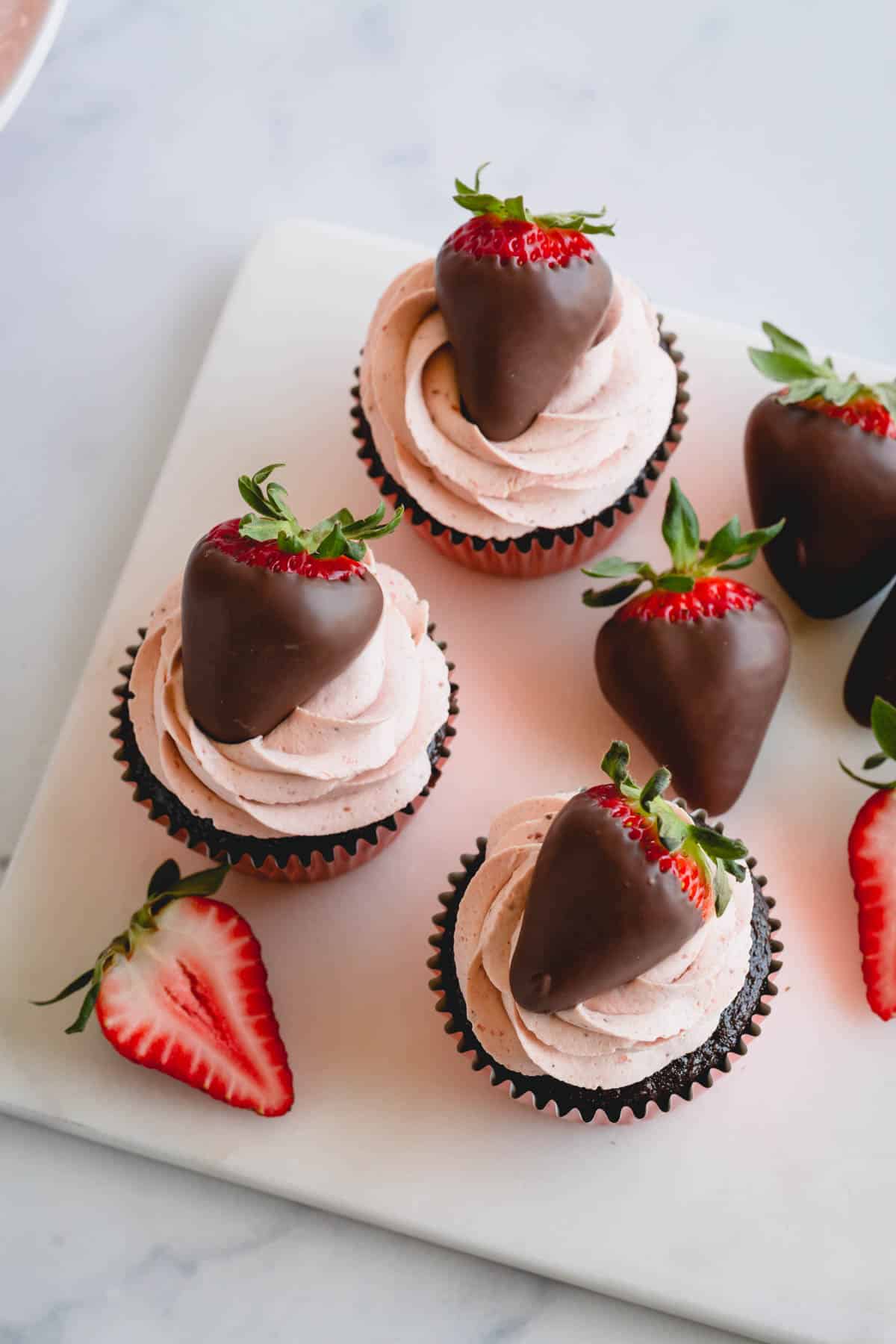 Three strawberry chocolate cupcakes topped with chocolate covered strawberries.