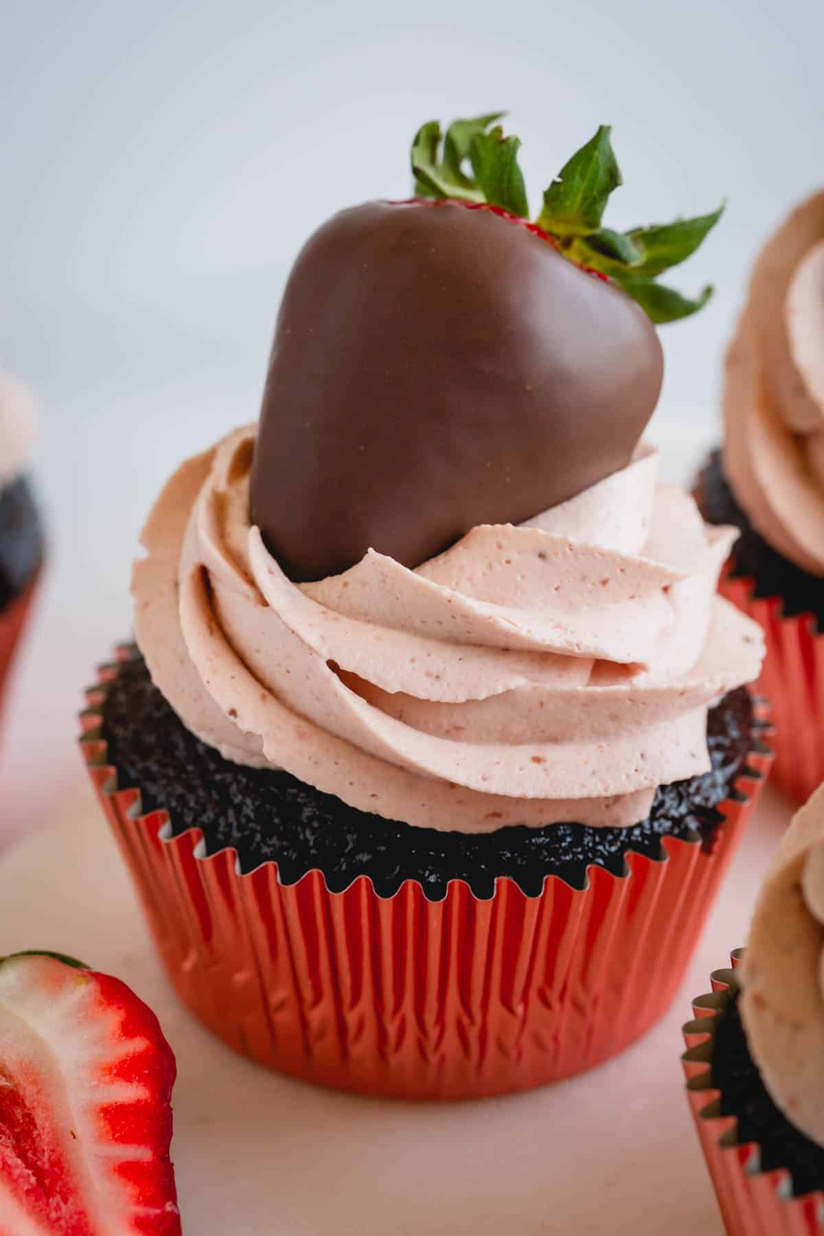 A chocolate cupcake topped with strawberry whipped cream frosting and a chocolate covered strawberry.