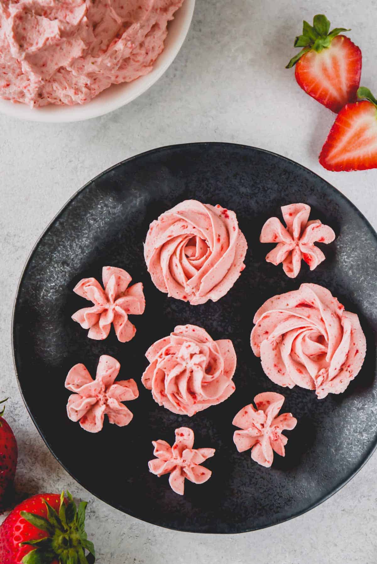 Overhead image of pink rosettes made of strawberry whipped cream frosting on a plate.
