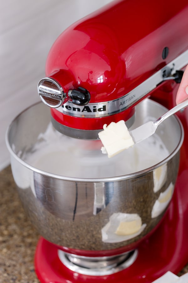 Adding a piece of butter into a stand mixer with meringue.