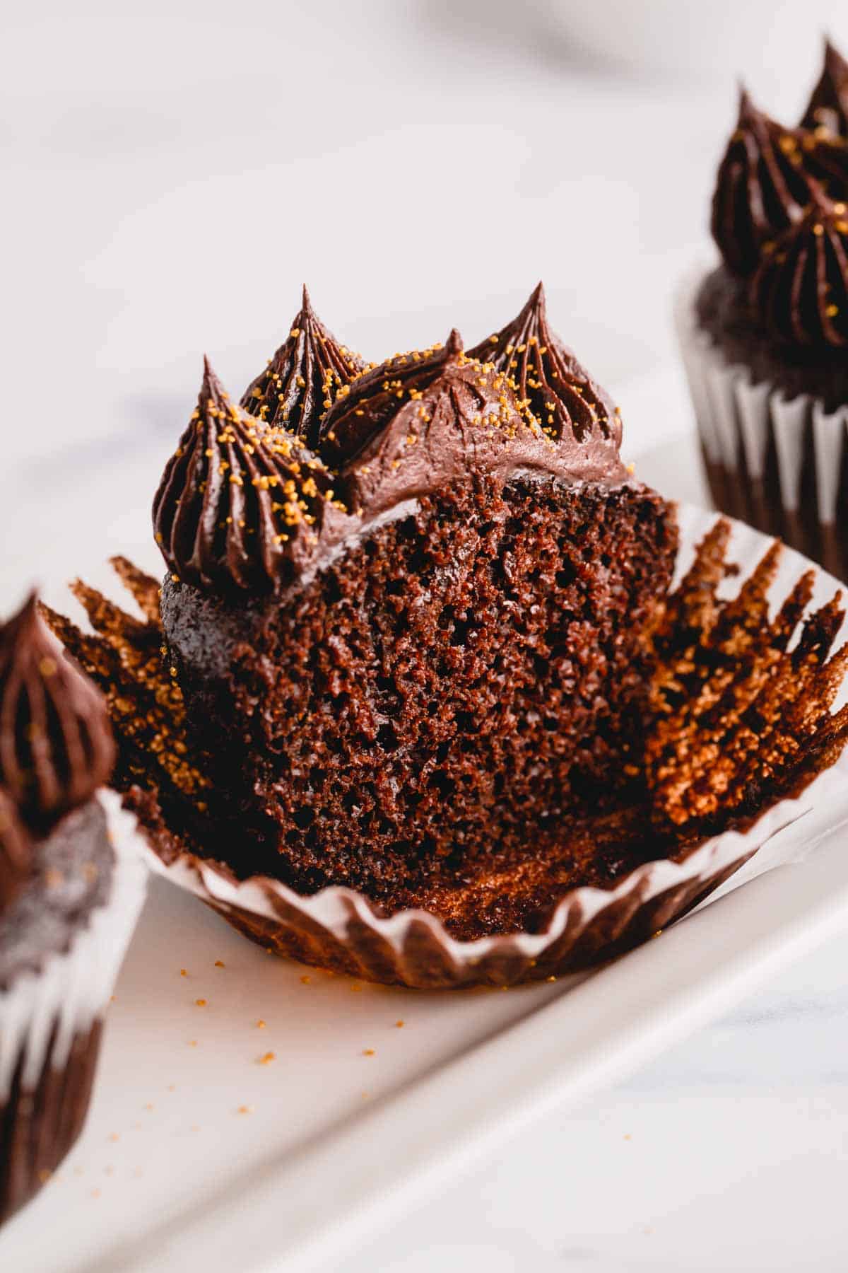 Half of an ultimate chocolate cupcake topped with chocolate frosting on a cupcake liner.