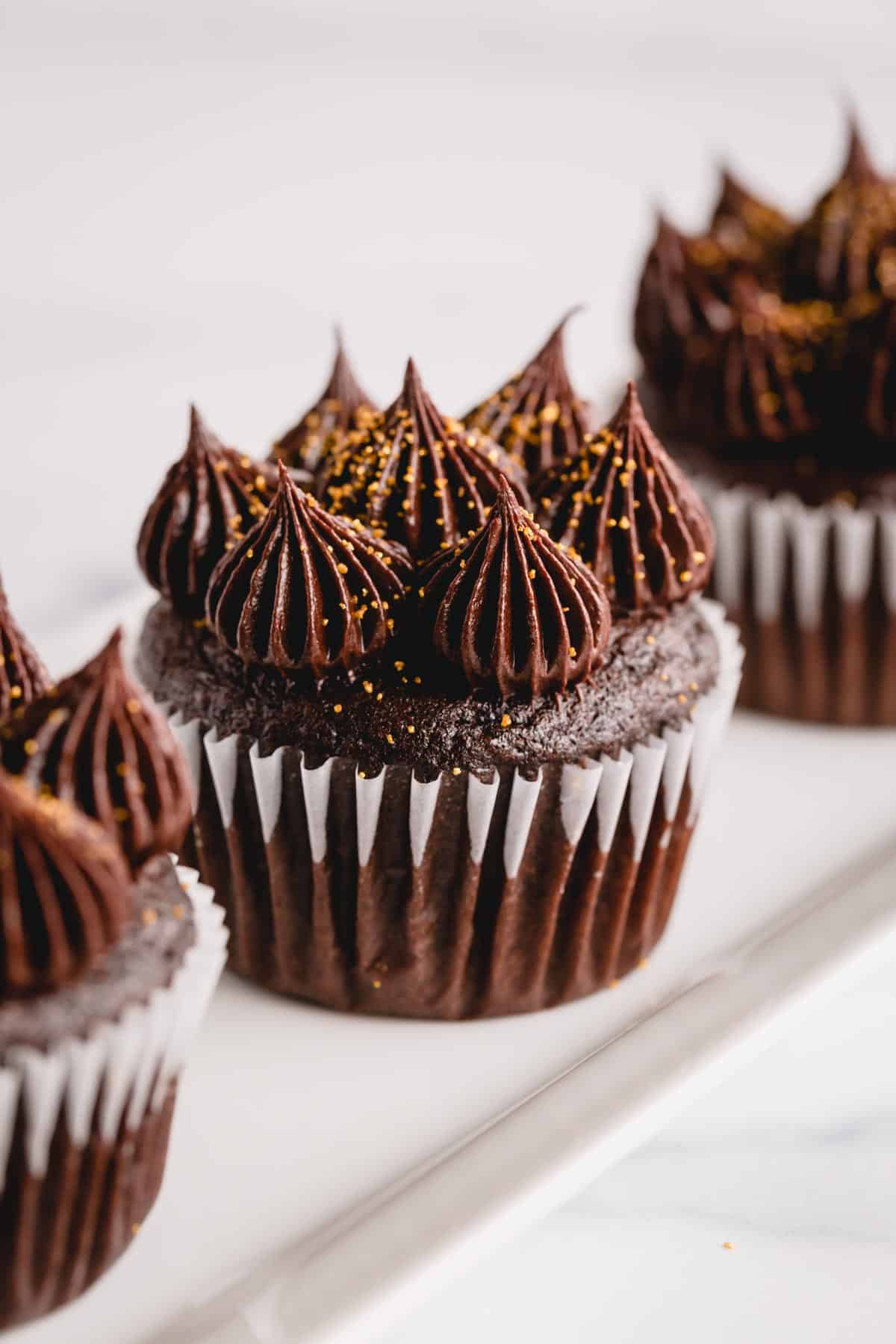 Three ultimate chocolate cupcakes topped with piped dollops of chocolate buttercream frosting.