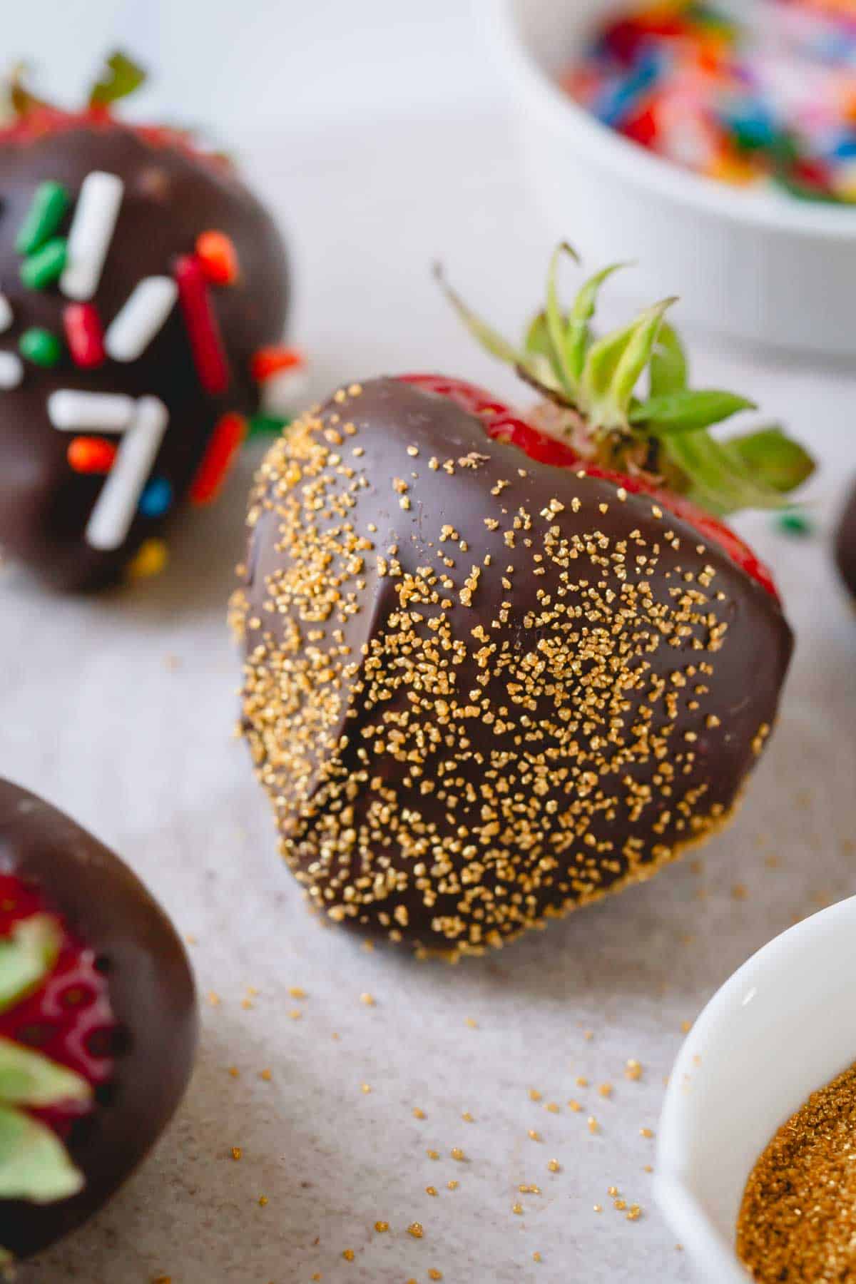 Close up image of a chocolate covered strawberry coated with small gold sprinkles.