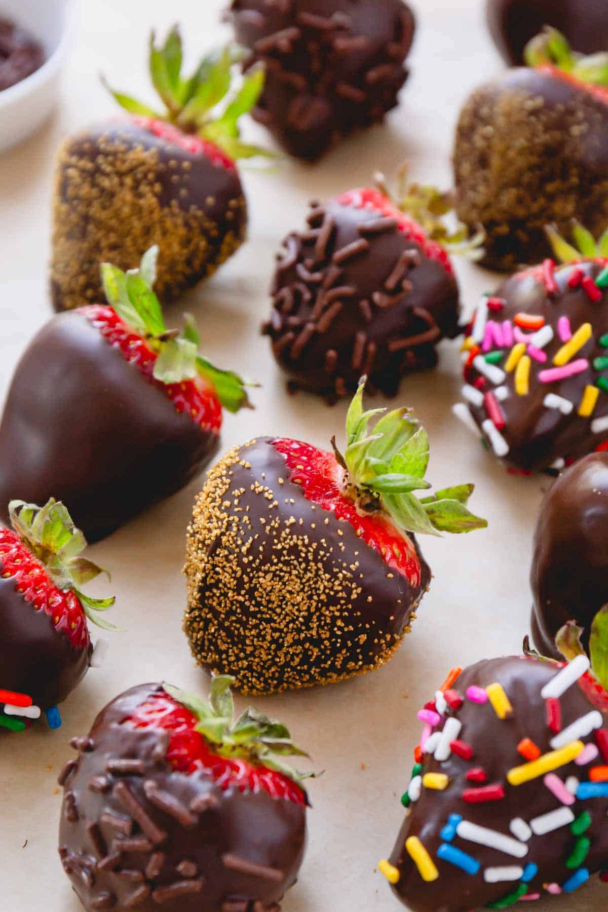 Chocolate covered strawberries coated with different sprinkles on a parchment paper-lined baking sheet.