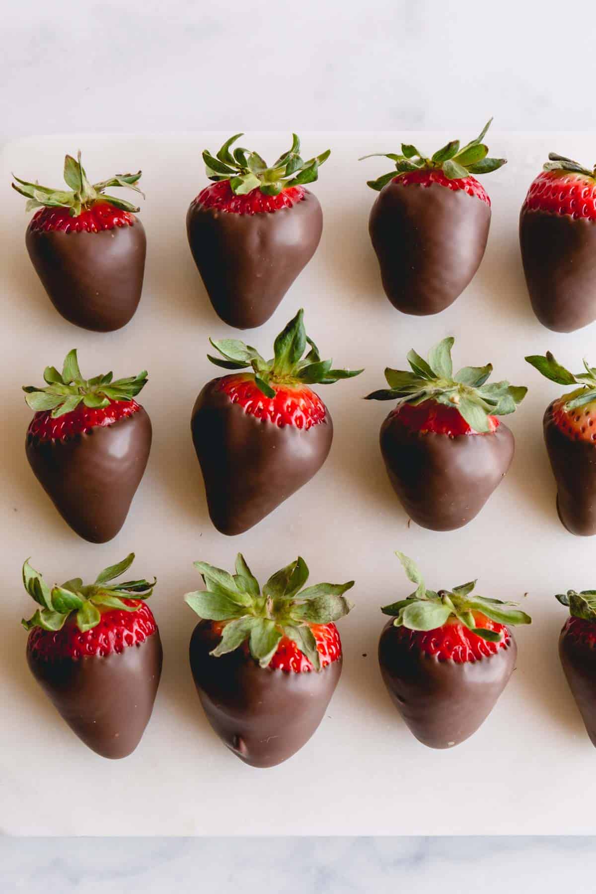 Three rows of chocolate covered strawberries on parchment paper.