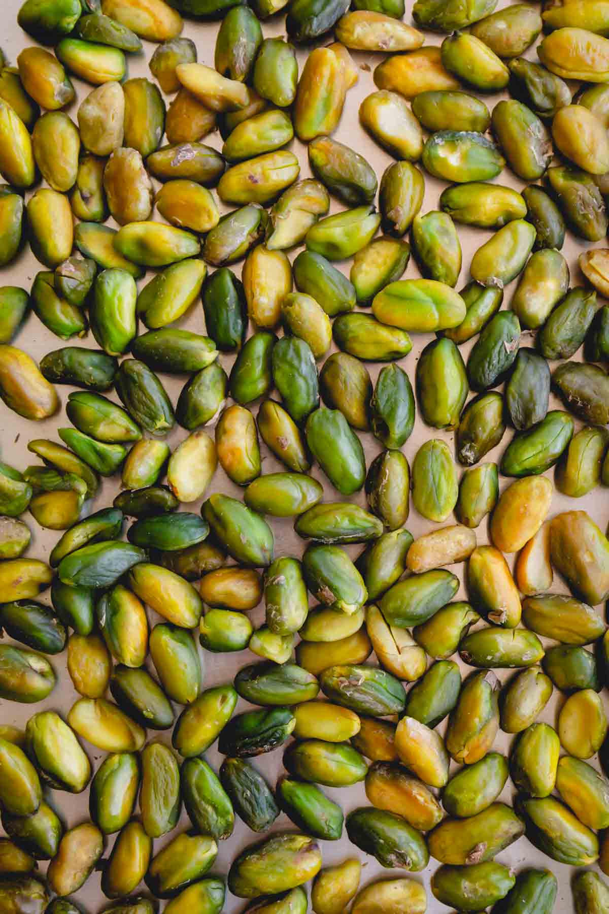 Blanched pistachios spread out in a single layer on a baking sheet.