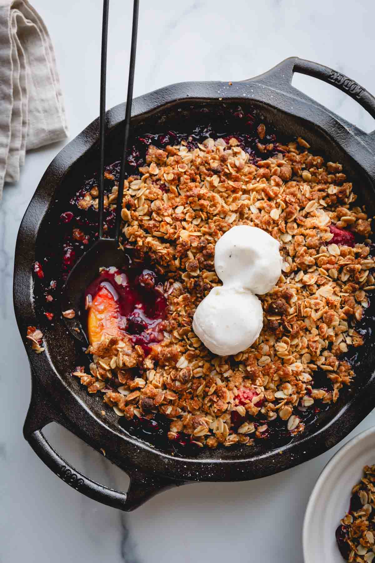 A skillet full of fruit crisp topped with two scoops of vanilla ice cream.